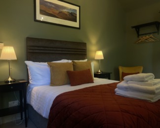 room 4's bed made up ready for guests. yellow and orange cushions, white towels on bed, green walls
