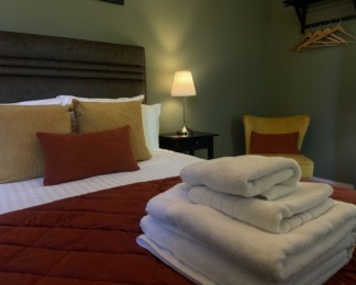 room 4 ready for guests to check in. green walls, white towels, orange and yellow cushions